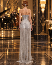 Load image into Gallery viewer, Silver Jazz Era gown featuring a structured crystal-embellished bodice with Art Deco geometric detailing and dramatic floor-length silver fringe.