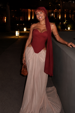 Load image into Gallery viewer, Woman wearing the Bordeaux Étoile Couture Gown featuring a structured Bordeaux corset, flowing champagne skirt, matching chiffon head scarf, and elegant floor-length silhouette.
