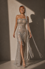 Load image into Gallery viewer, Woman wearing the Celestial Fringe Couture Gown featuring crystal-inspired embroidery, shimmering beaded fringe, a strapless neckline, fitted silhouette, and elegant side slit.