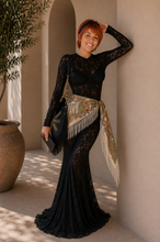 Load image into Gallery viewer, Woman wearing the Noir Riviera Lace Set featuring a fitted black floral lace maxi silhouette with a printed scarf belt, styled with a black fringe handbag for a luxury resort and editorial fashion look inspired by the French Riviera.