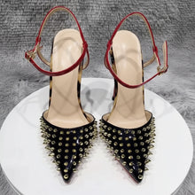 Load image into Gallery viewer, Black pointed-toe stiletto pumps with gold stud embellishments, red patent ankle straps, and sculptural metallic heels displayed in a luxury fashion setting.