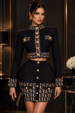 Load image into Gallery viewer, Black and gold structured two-piece women's set featuring a cropped long-sleeve jacket with geometric trim and matching high-waisted mini skirt.