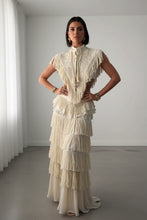 Load image into Gallery viewer, Woman wearing a luxury embroidered fringe cape with botanical detailing and a stand collar in a minimalist architectural setting.