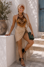 Load image into Gallery viewer, Woman wearing the Nomad Soleil look featuring a handcrafted wooden beaded statement top, embroidered fringe wrap skirt, emerald fold clutch, and elegant resort styling inspired by Mediterranean luxury.