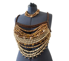 Load image into Gallery viewer, Woman wearing the Nomad Soleil look featuring a handcrafted wooden beaded statement top, embroidered fringe wrap skirt, emerald fold clutch, and elegant resort styling inspired by Mediterranean luxury.